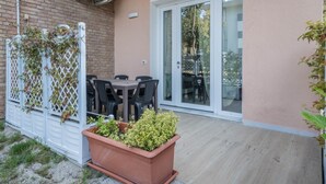 A patio with a table and chairs, a potted plant, a brick wall, and an air conditioning unit. - Appartamento Andromeda 13 (Bibione)