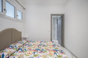 A bedroom with a bed, a window, a door, and a small white air conditioning unit.