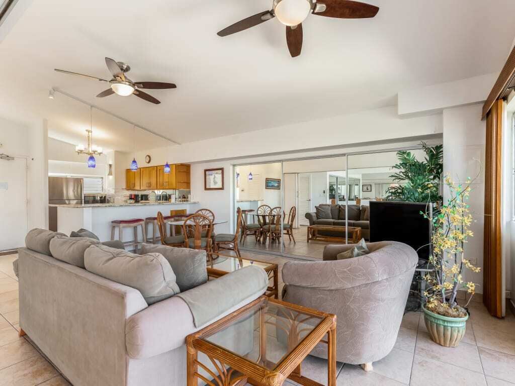 Un grand espace de vie comprenant un canapé, une table basse et une table à manger avec des chaises. Au fond, on trouve une cuisine équipée de placards et d’un réfrigérateur.
