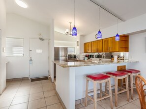 A kitchen with a central island, wooden cabinets, and bar stools.