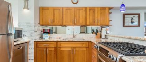 A modern kitchen with wooden cabinets, a stainless steel refrigerator, a built-in oven, and a granite countertop.