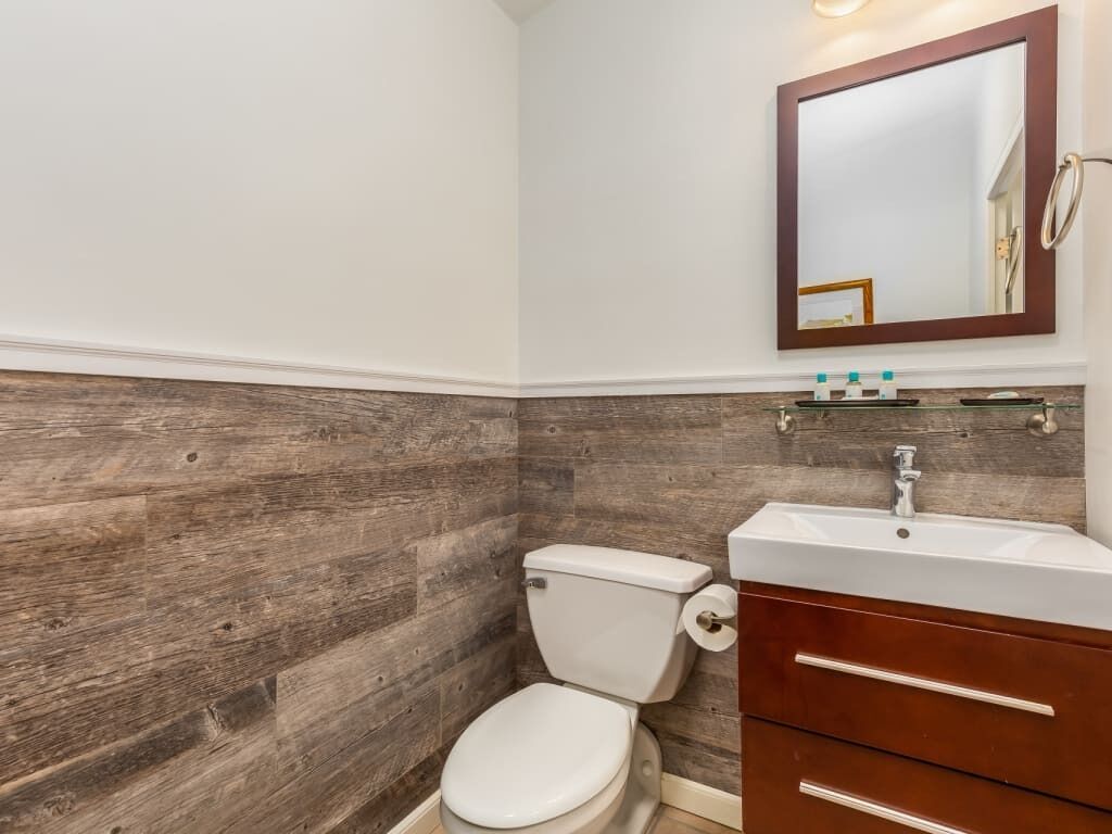 A bathroom with a wooden wall, a white toilet, a white sink, and a mirror above the sink.
