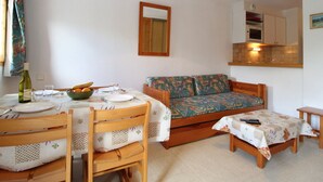 A compact living space with a dining table set for two, a sofa, a small table, and a kitchenette in the background. - Cozy 4-Person Ski-in/Ski-out Apartment with Balcony, Free WiFi, and Garage in Val Cenis (Termignon)