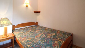 A small, simple room with a single bed, a nightstand, a lamp, and a wall-mounted light fixture. - Cozy 4-Person Ski-in/Ski-out Apartment with Balcony, Free WiFi, and Garage in Val Cenis (Termignon)