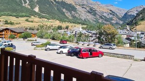 A parking lot with several cars, a mountain backdrop, and a small town with buildings and a church. - Cozy 4-Person Ski-in/Ski-out Apartment with Balcony, Free WiFi, and Garage in Val Cenis (Termignon)