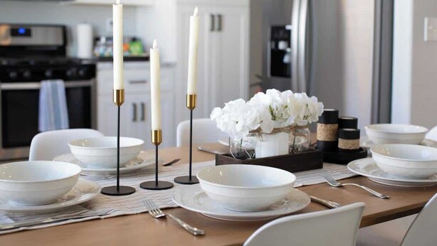 A dining table set with white plates, bowls, and cutlery, candles, and a vase with white flowers. - Modern 3 BR Home w/ Hot Tub, Pool, Golf! (North Las Vegas)