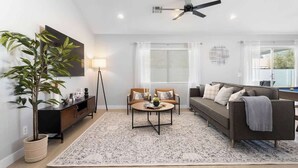 A modern living room with a sofa, a coffee table, and a floor lamp. - Modern 3 BR Home w/ Hot Tub, Pool, Golf! (North Las Vegas)