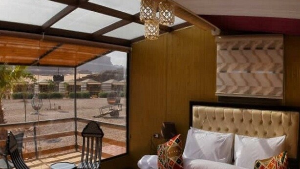 A bedroom with a large window, a bed with white linens, and a view of the desert landscape.