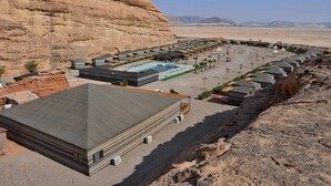 A hotel with a pool, outdoor seating, and a desert backdrop.