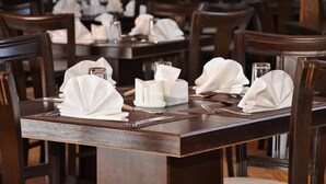 A restaurant setting with neatly arranged tables, each with folded white napkins, glassware, and cutlery.