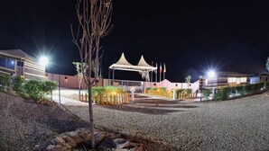 A well-lit outdoor area with a covered seating area, a flagpole, and a building with multiple windows.