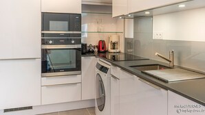 A modern kitchen with white cabinetry, a built-in oven, a microwave, a coffee maker, and a stainless steel sink.
