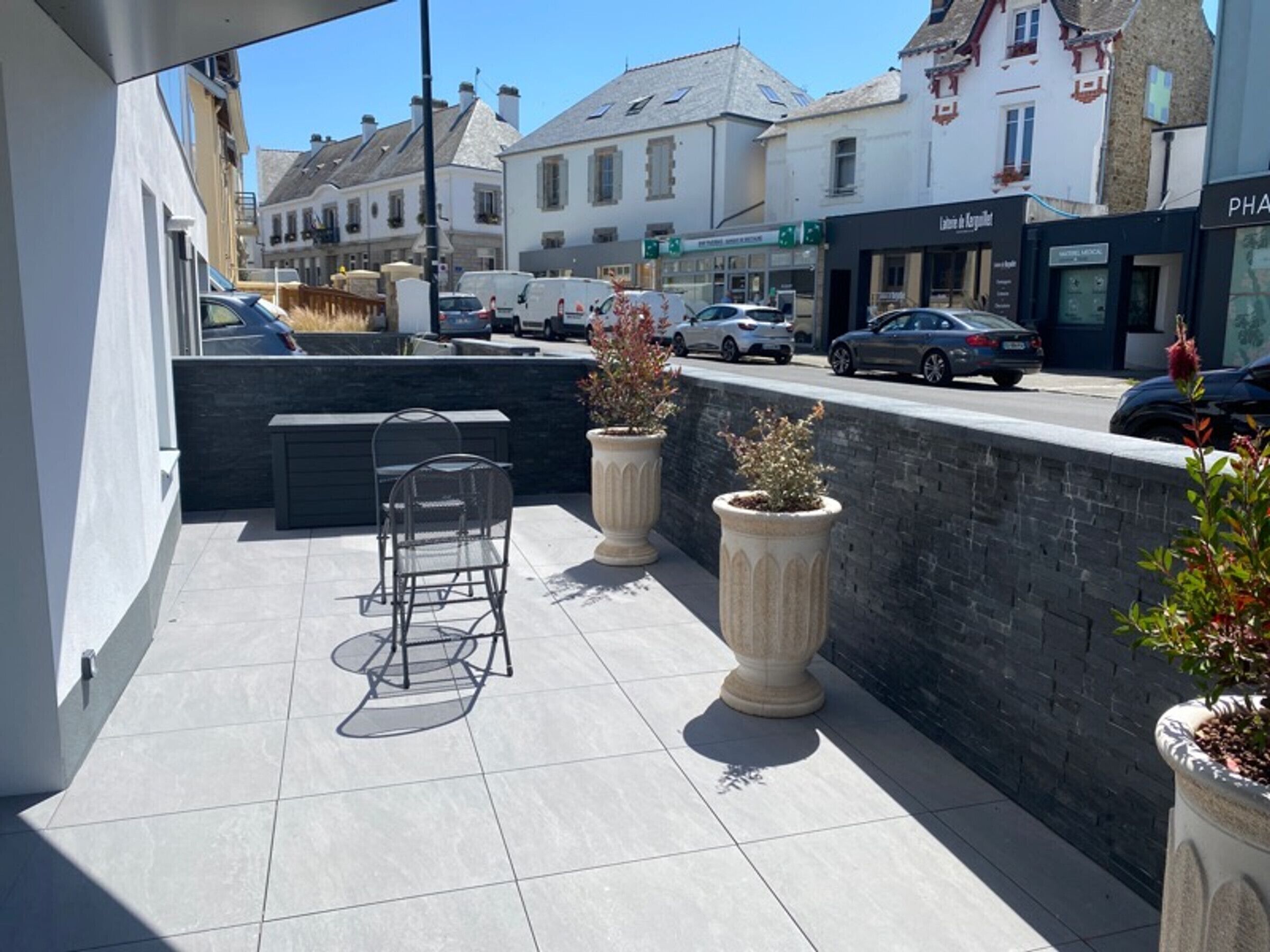 Un patio exterior con zona de estar, plantas en macetas y vistas a la calle y edificios.