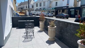 An outdoor patio with a seating area, potted plants, and a view of the street and buildings.