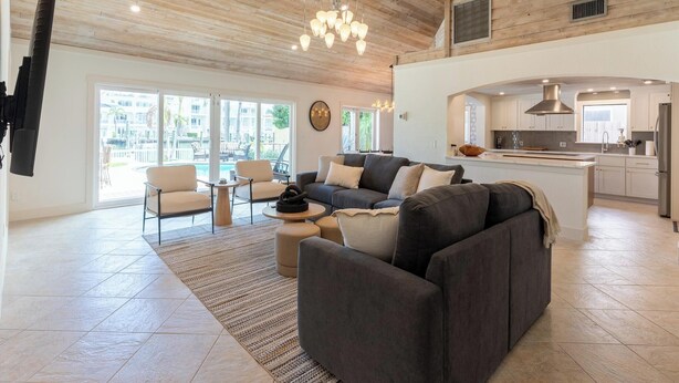 Amplia sala de estar con una cocina moderna, ventanas grandes y un techo alto con vigas a la vista.