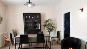 A dining area with a wooden table and black chairs, a black cabinet with glassware, a potted plant, and a vase with flowers.