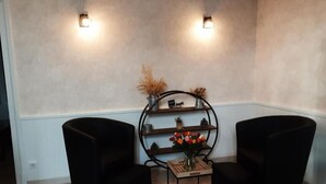 A corner seating area with two black chairs, a small table with a vase of flowers, and a metal shelf with decorative items.