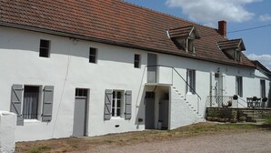 A white building with a red-tiled roof, multiple windows, and a staircase leading to a porch area.