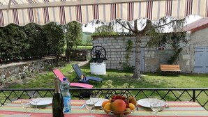 An outdoor dining area with a table set for four, surrounded by chairs, a fruit bowl, and a bottle of water.