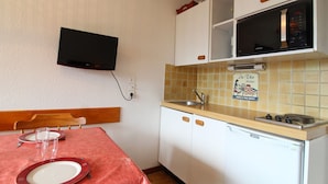 Cocina compacta con gabinetes blancos, microondas y un lavamanos pequeño. Un televisor está montado en la pared sobre la encimera.
