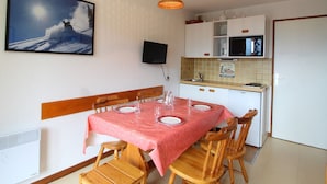 Comedor con una mesa dispuesta para cuatro, un televisor montado en la pared y una cocina con microondas y armarios.