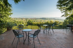 Une terrasse avec des sièges extérieurs, une vue sur un paysage rural et une clôture en métal.