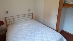 A single bed with a wooden headboard in a room with white walls and a wooden door. - Spacious 3 Rooms + Mountain Alcove, Sleeps 6/8, Close to Ski Lift and Shops (Valfréjus)