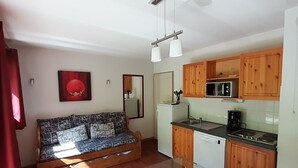 A compact living space with a sofa, a small dining table, a kitchenette, and a red curtain. - Spacious 3 Rooms + Mountain Alcove, Sleeps 6/8, Close to Ski Lift and Shops (Valfréjus)