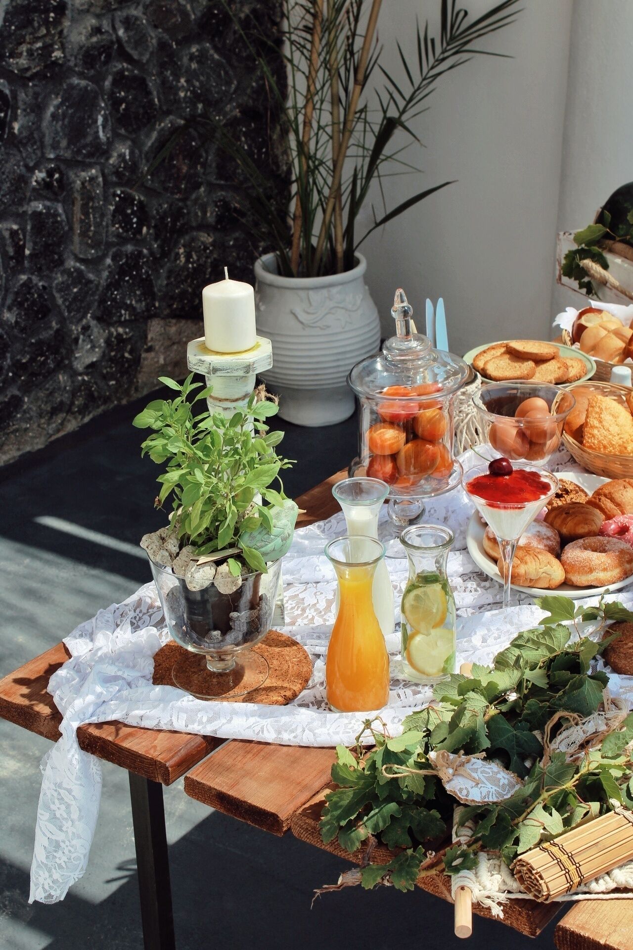 Una mesa al aire libre con diversos alimentos, una vela y una planta en maceta.