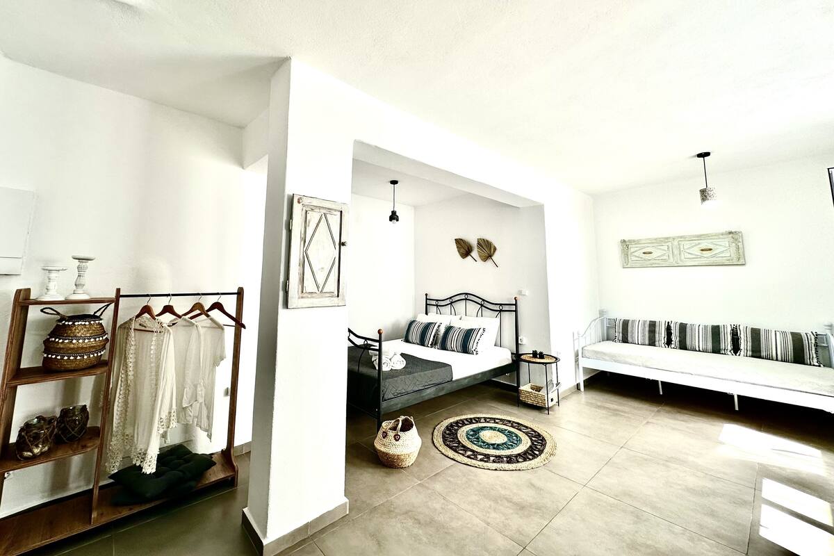 A spacious living area with a sofa, a bed, and a small table. There are decorative items on shelves and a wall-mounted shelf.