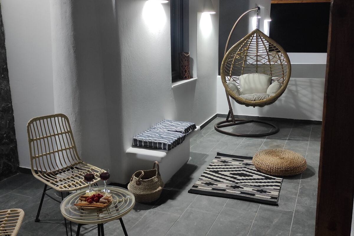 A cozy outdoor seating area with wicker chairs, a hanging chair, and a small table with snacks and drinks.