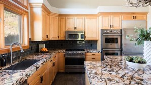 A modern kitchen with wooden cabinets, a granite countertop, stainless steel appliances, and a large window. - Nansen Villa (Park City)