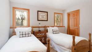 A bedroom with two wooden beds, white bedding, a nightstand with a lamp, and framed artwork on the wall. - Nansen Villa (Park City)