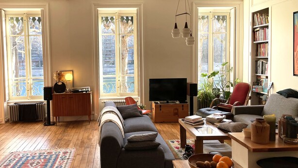 A cozy living room with a sofa, a coffee table, a bookshelf, and a television. - Spacious 120 m2, 4 bedrooms with garages and Saône view. (Lyon)