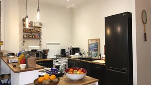 A modern kitchen with a black refrigerator, stove, and dishwasher. There are oranges and a bowl of fruit on the counter. - Spacious 120 m2, 4 bedrooms with garages and Saône view. (Lyon)