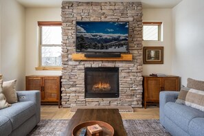 A living room with a stone fireplace, a flat-screen TV mounted above it, and two sofas. - Trailhead  721 Pet Friendly pool hot tub (Winter Park)