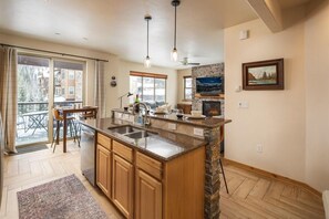 A spacious kitchen with a large island, a dining area with chairs, a fireplace, and a view of the outside. - Trailhead  721 Pet Friendly pool hot tub (Winter Park)