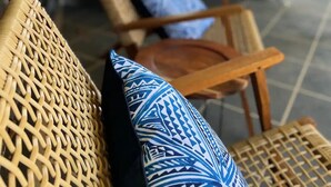 Muebles de mimbre con cojines estampados azules, una pequeña mesa redonda y una zona de patio con pared de ladrillo y asientos exteriores.