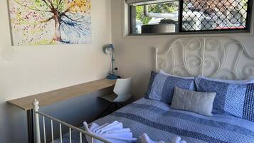 A bedroom with a bed, a window with a view, a painting on the wall, and a desk with a chair.