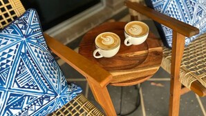 Una silla de madera con una mesa redonda, dos tazas de café y cojines estampados.