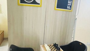 Una habitación con un separador de madera, dos sillas de plástico negro y un tablero de ajedrez.