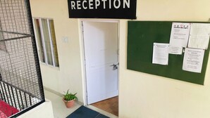 Zona de recepción con un cartel, una puerta, un tablón de anuncios y dos plantas en macetas.