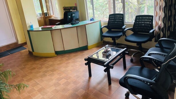 Zona de recepción con escritorio, sillas, máquina de café y ventana con vista a árboles.