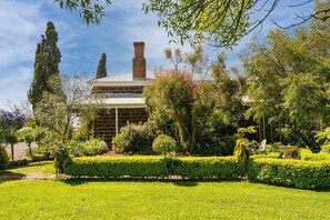 Una casa in mattoni dal design tradizionale, con un camino, circondata da giardini curati e alberi.