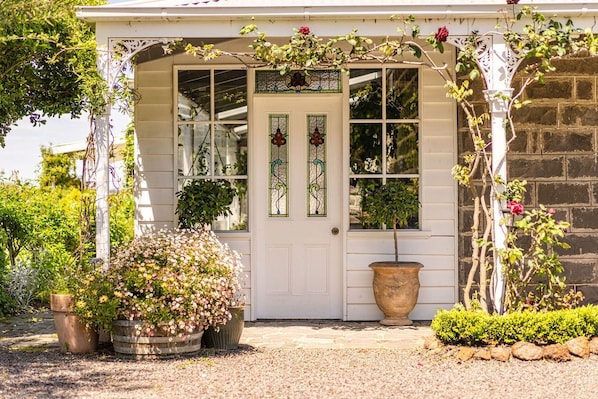 Una casa bianca con un portico bianco, un vaso di fiori grande e un piccolo giardino.