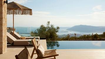 A poolside area with lounge chairs and a view of the sea and mountains.