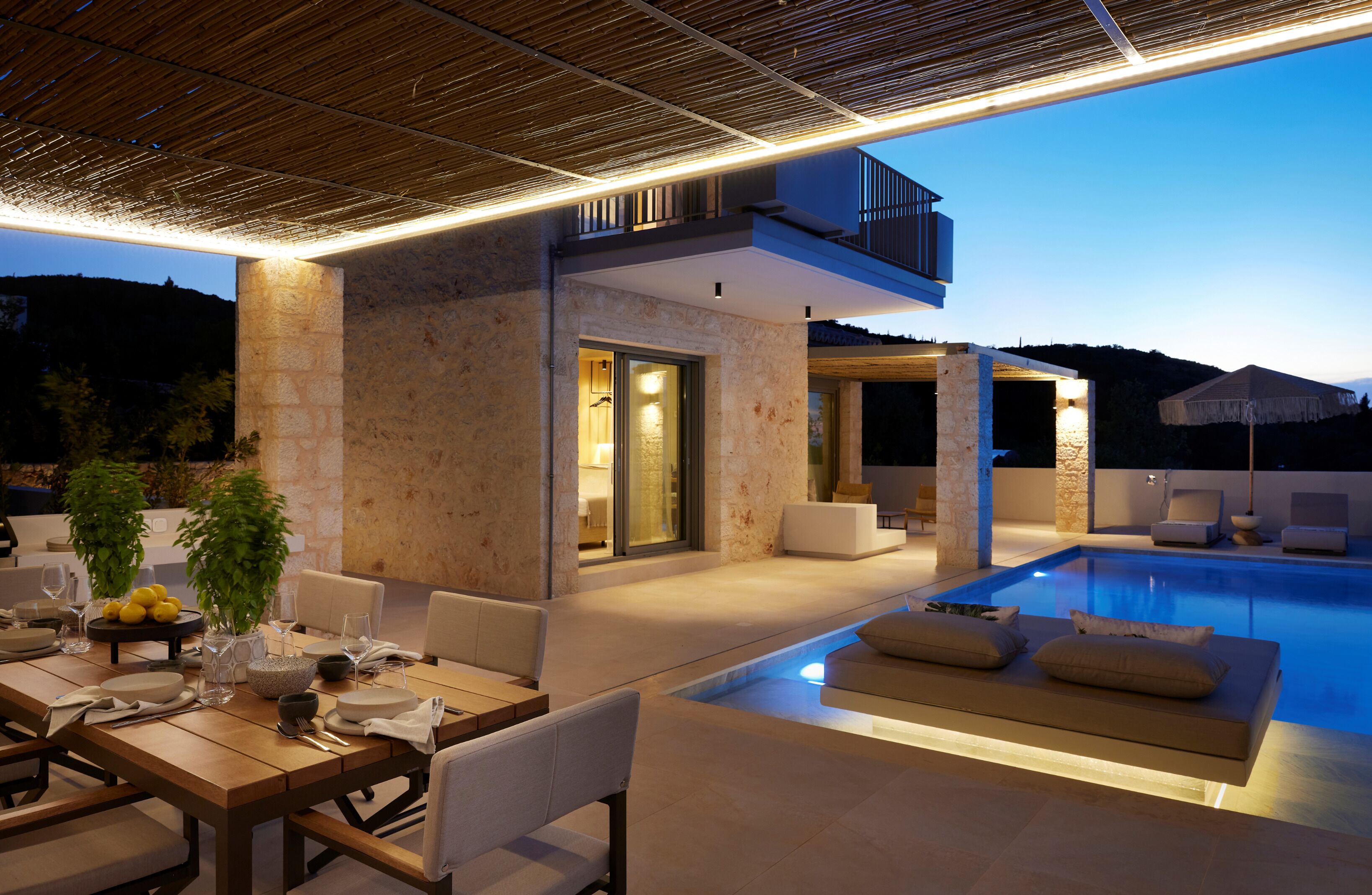 Ein moderner Poolbereich im Freien mit Essbereich, inklusive Tisch und Stühlen, sowie einer Lounge-Ecke mit Kissen.