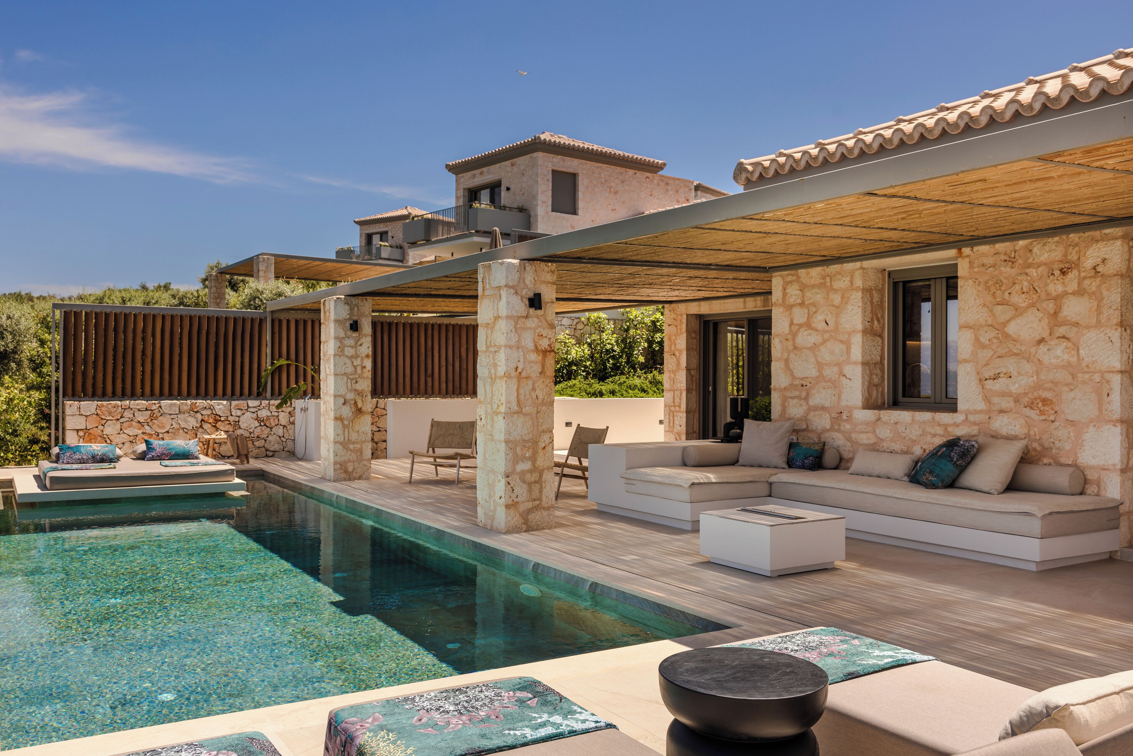 A modern outdoor pool area with stone walls, a covered seating area, and a view of neighboring buildings.