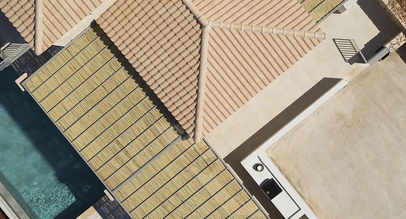 Une vue aérienne d’un hôtel doté de plusieurs toits recouverts de tuiles, d’une piscine et d’un bâtiment séparé avec une fenêtre circulaire.