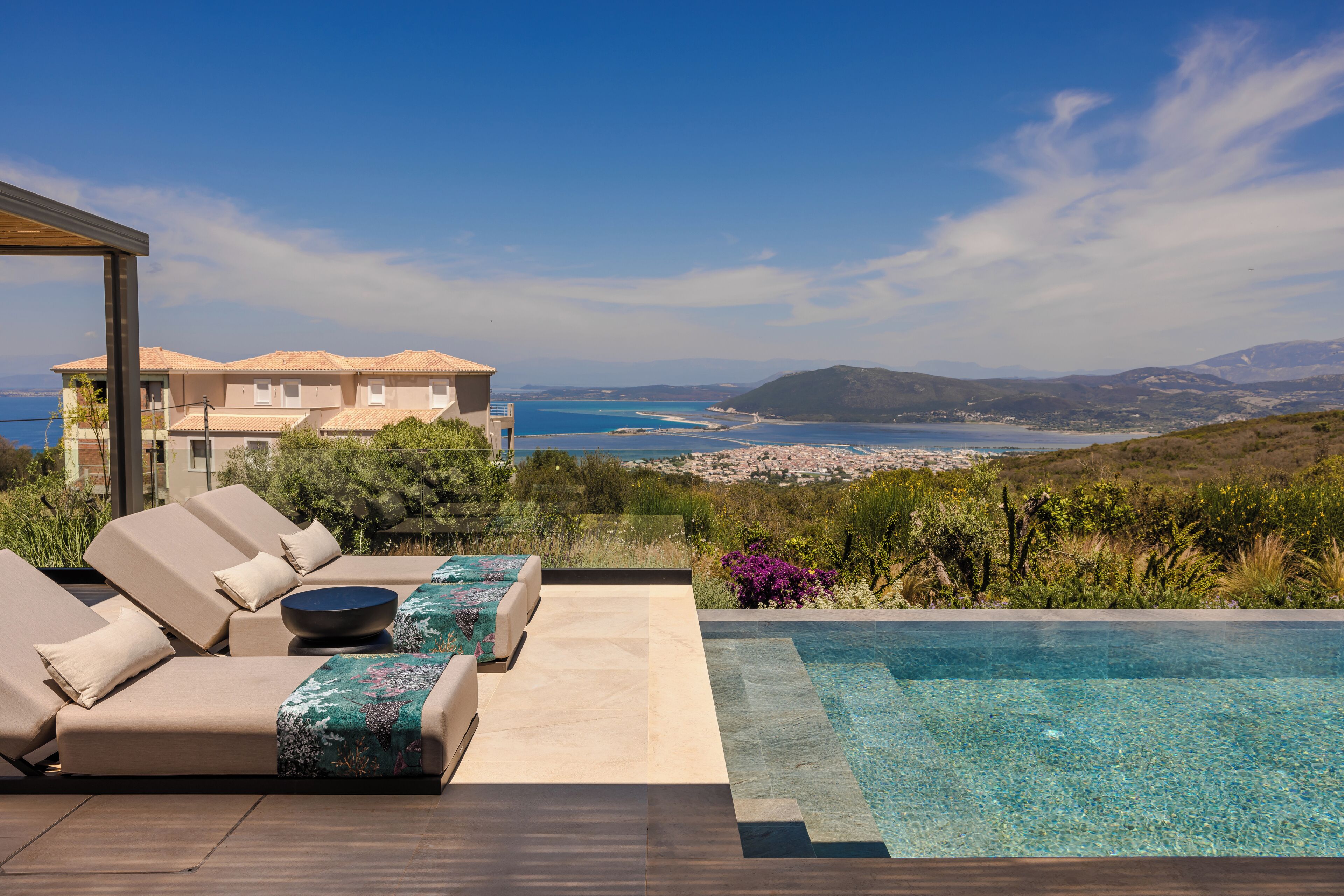 Un espace aménagé au bord de la piscine, avec des chaises longues et une vue sur la mer et les collines lointaines.
